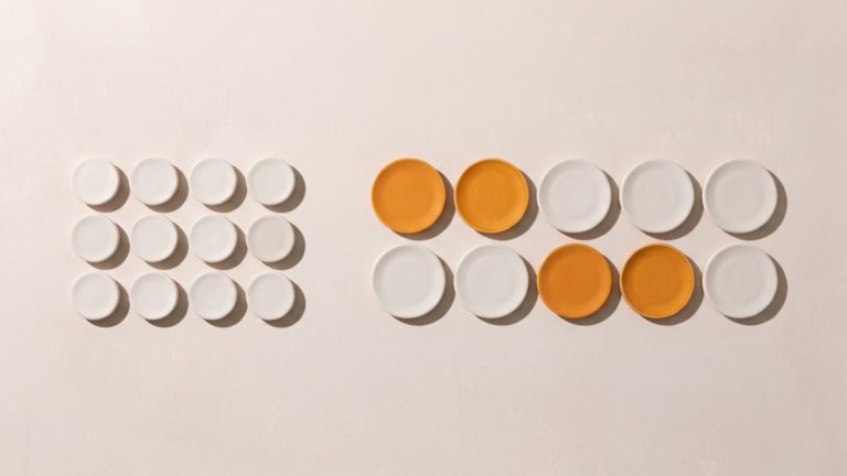 Two groups of ceramic plates on a light surface: twelve small white ones on the left, ten larger ones on the right, four of them orange Two groups of ceramic plates on a light surface: twelve small white ones on the left, ten larger ones on the right, four of them orange